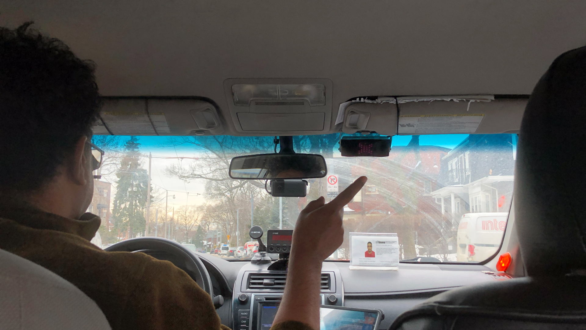 The windshield of a car with a man in the driver seat pointing to the right