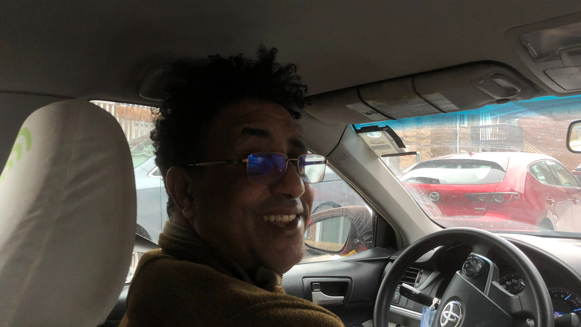 A man sitting in the front seat of a car and facing to the back smiling