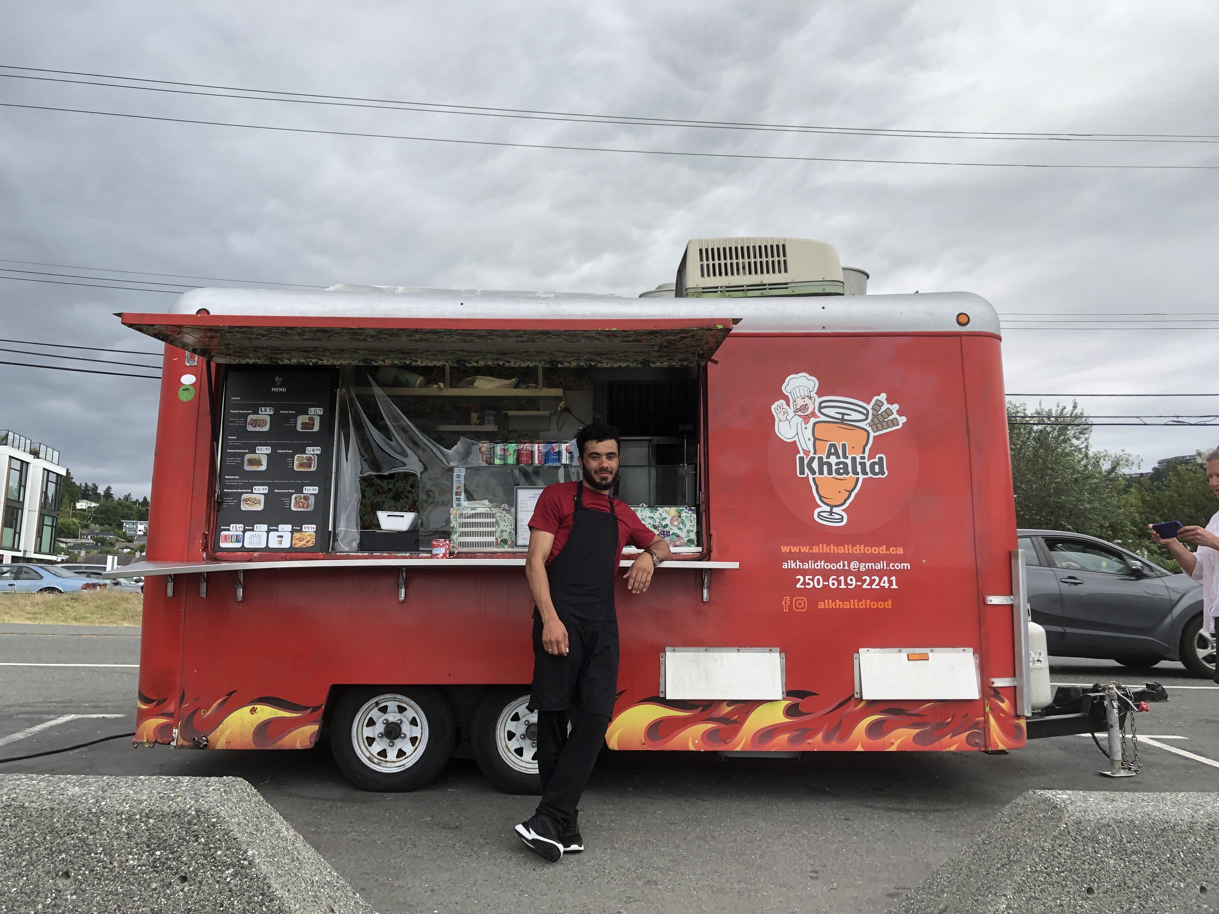 A man with a black apron standing in front of a red food truck