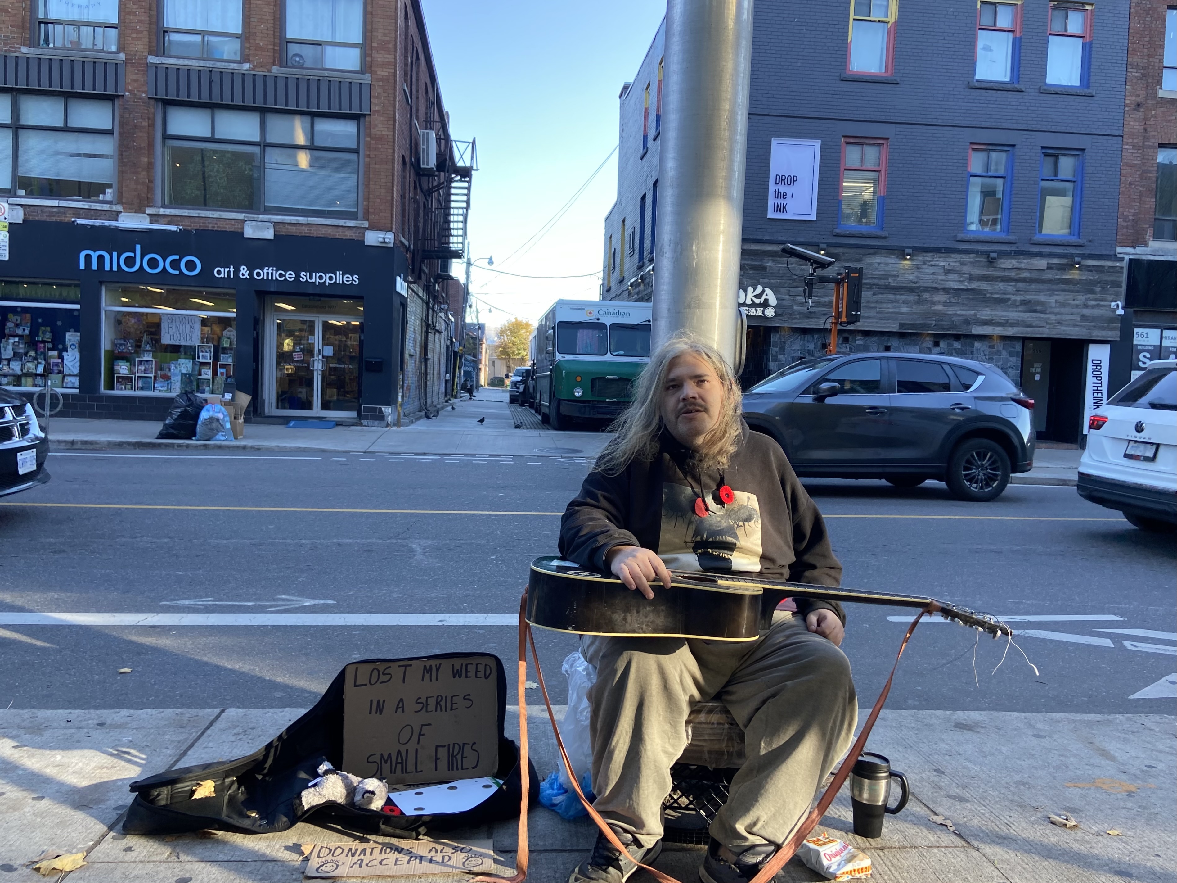 A person sits on the sidewalk with a guitar in their lap