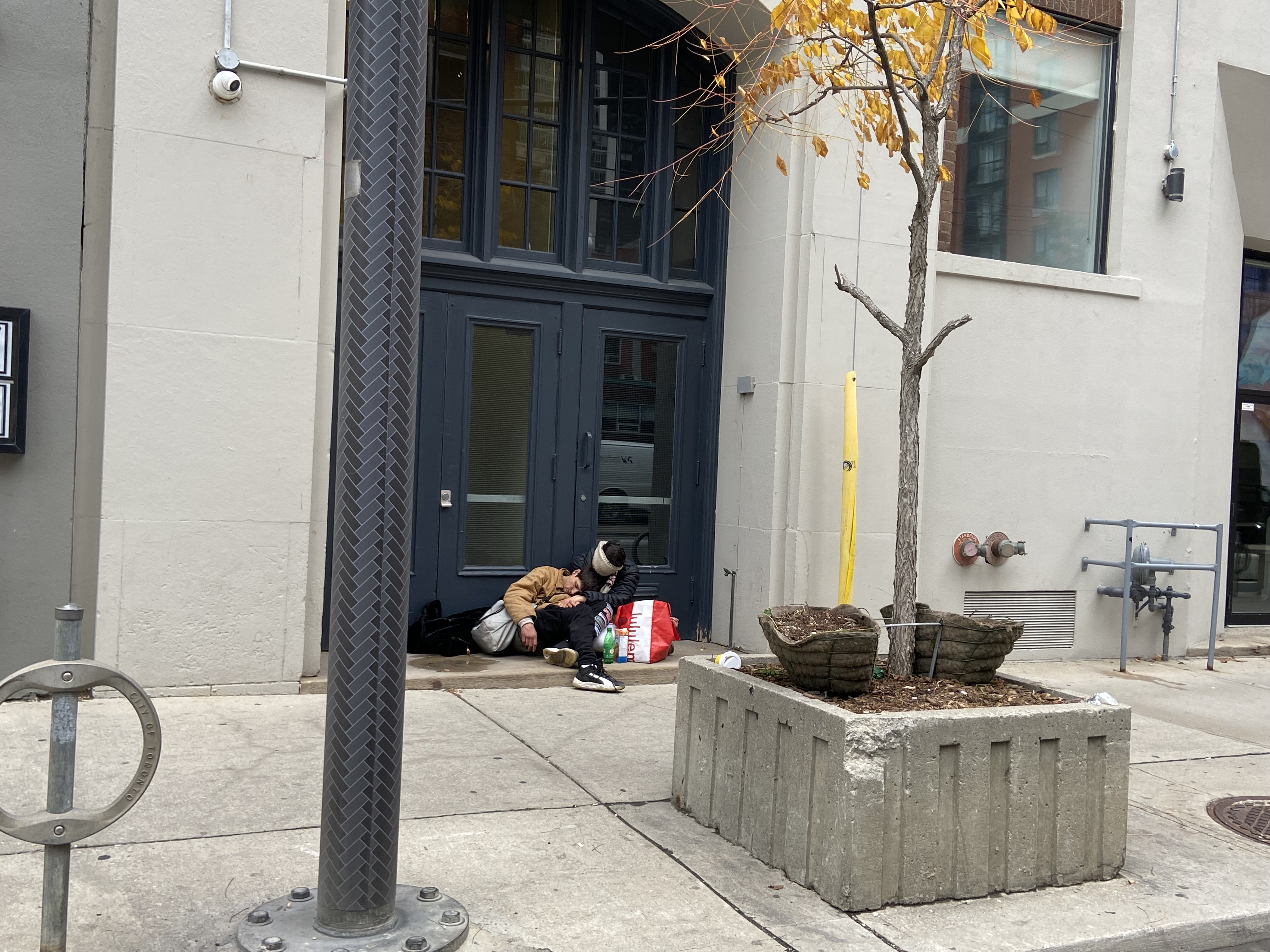 Two people sit slumped together on stoop of doorway off the sidewalk