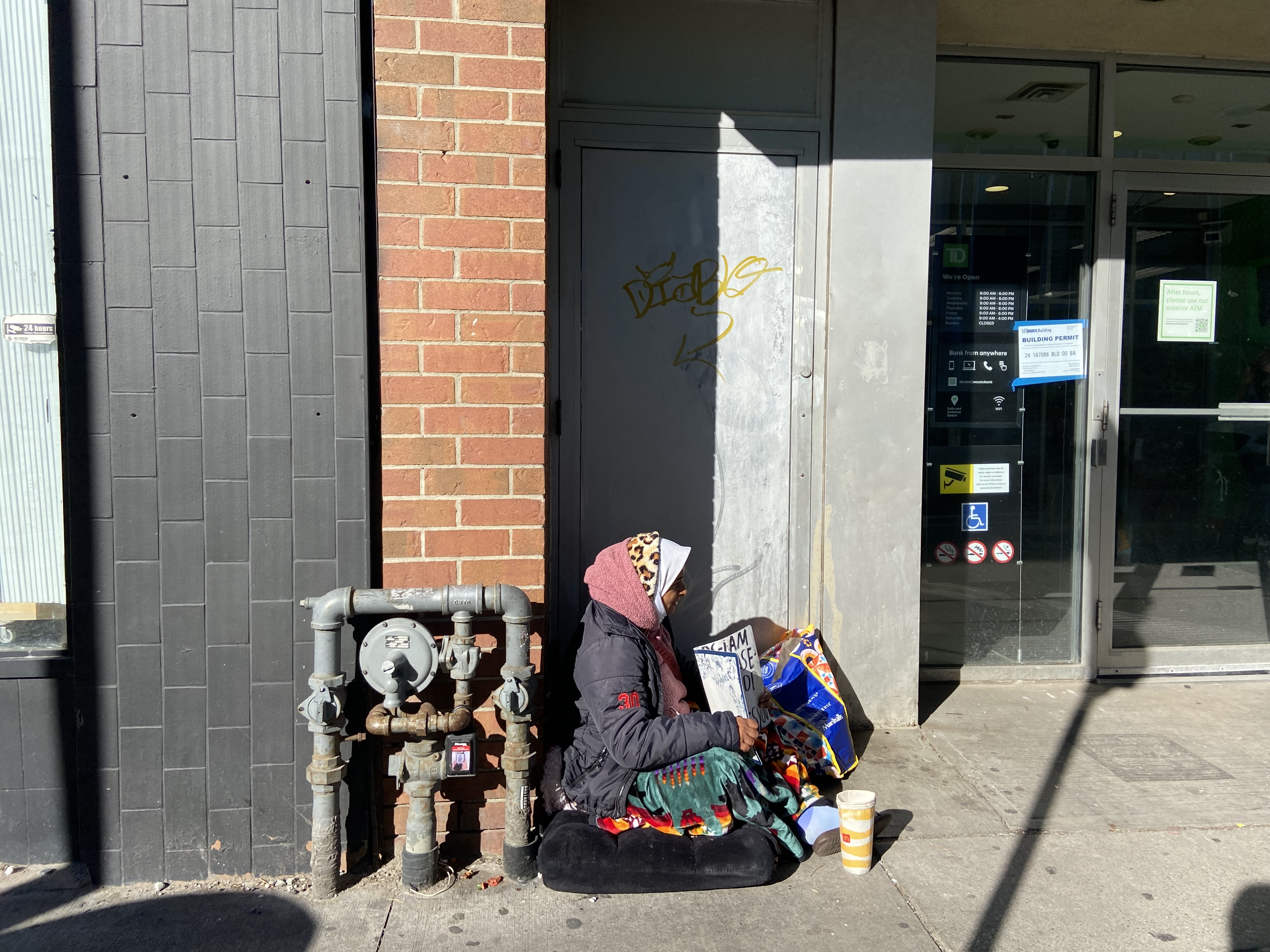 A woman wearing many layers of clothing sits on the sidewalk